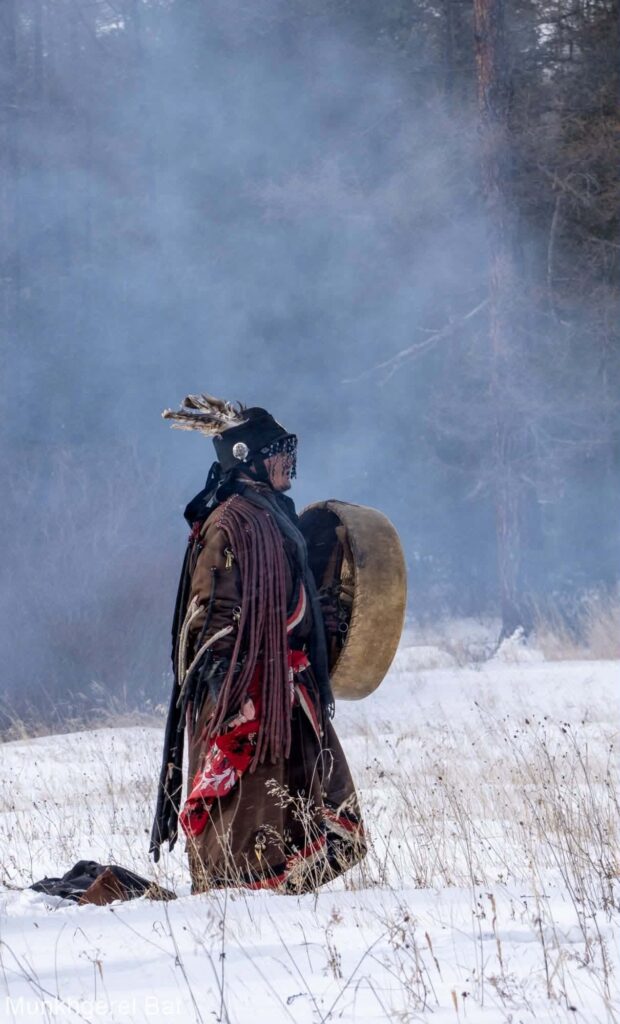 Chamane mongol en costume rituel, avec son tambour, dans la neige et la fumée